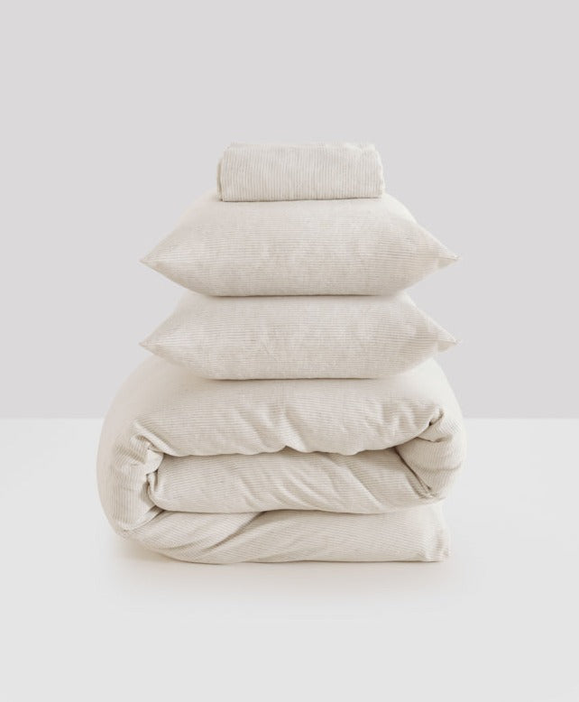 Four neatly stacked MOST washed linen pillows and a duvet in off-white, set against a clean, light grey background.