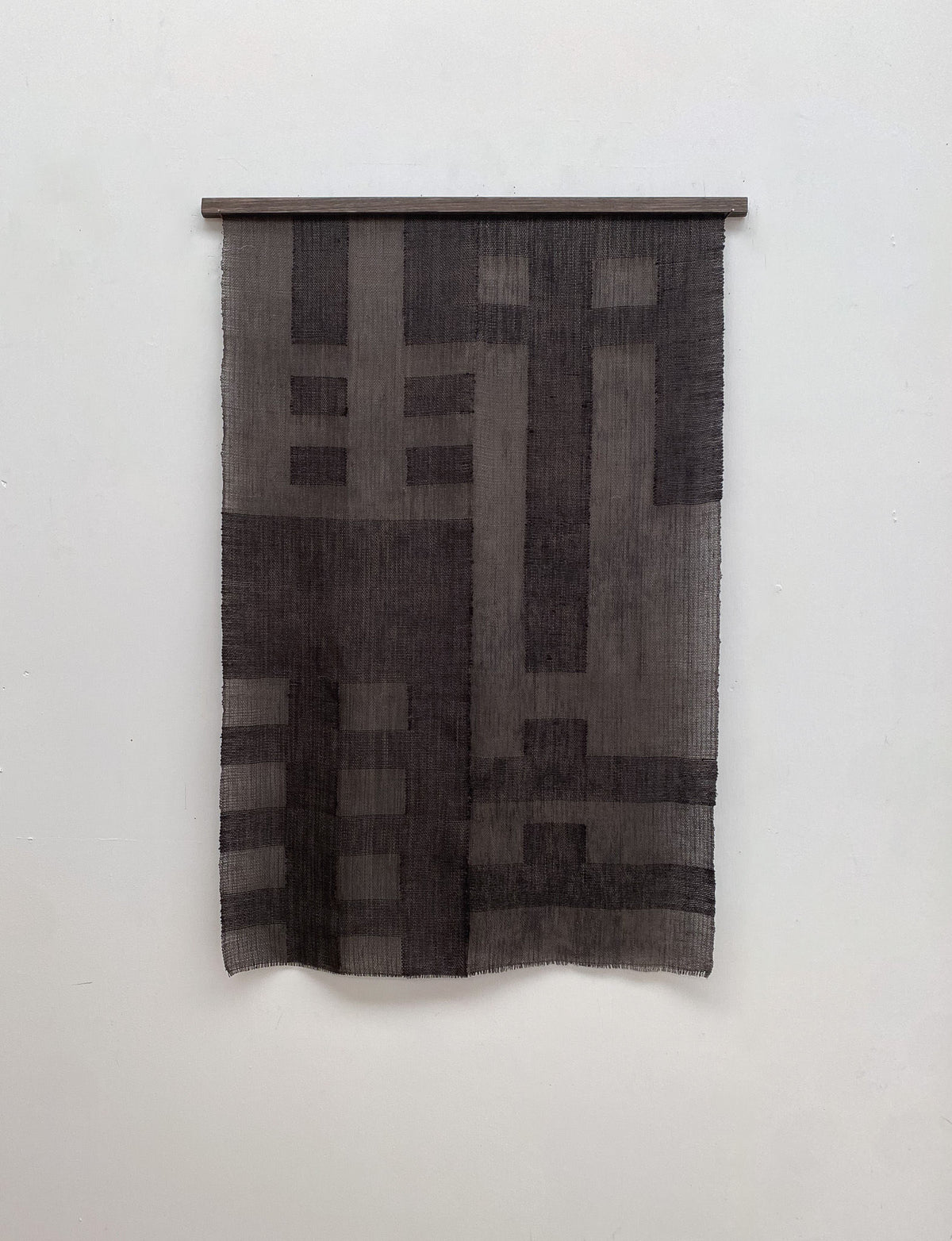 The Grid I tapestry by Sundance Studio, inspired by the Bauhaus movement, hangs on a wall. It features geometric rectangles and lines in textured gray for a modern, minimalist look.