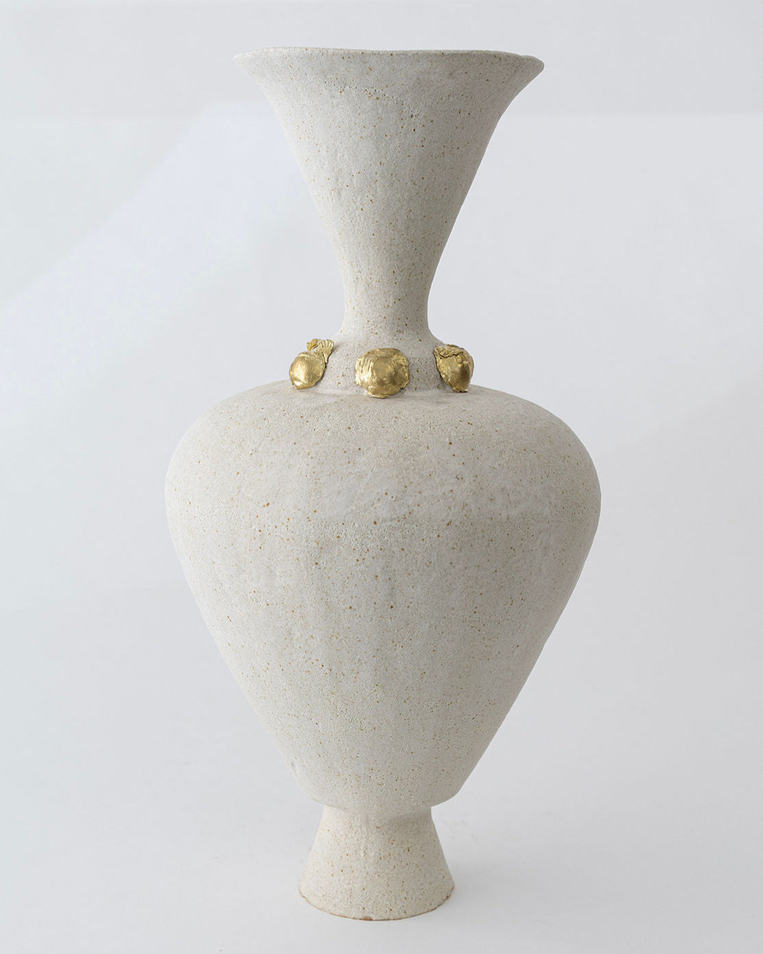 The Isolated n.24 Vase by Canoa Lab is a tall, light beige ceramic piece with a wide flared mouth, narrow neck, and four small gold accents at the base of the neck. Mediterranean-inspired design shown against a plain white background.