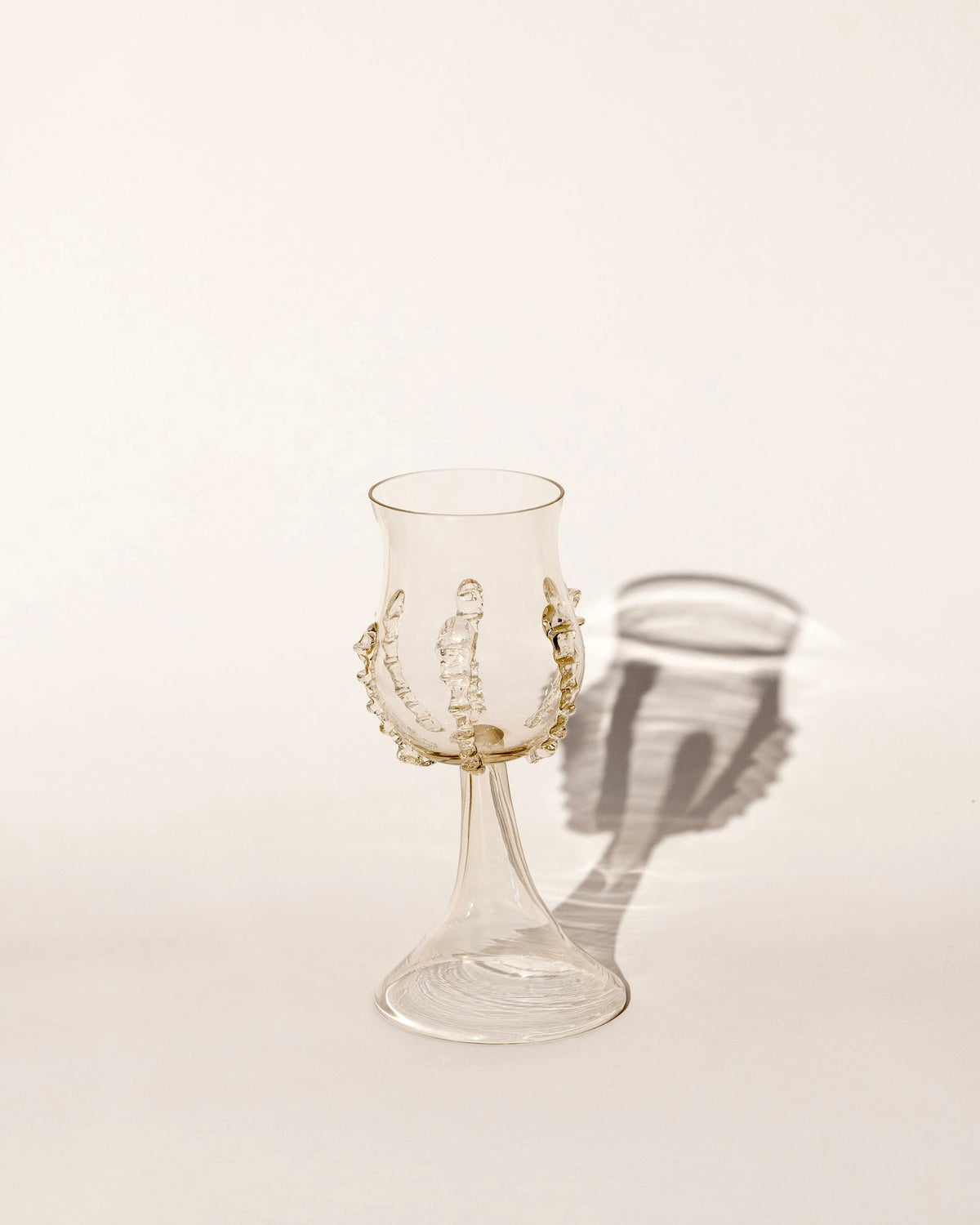 A pair of mouthblown ribbed wine goblets by Lucie Claudia Podrabska cast soft shadows on a neutral, light background.
