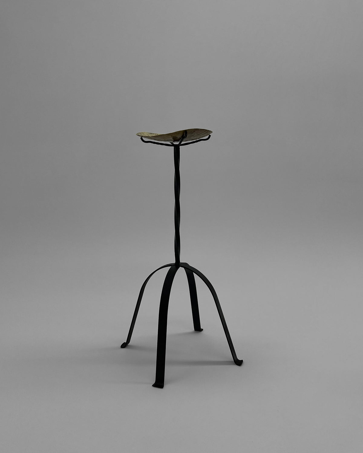 Minimalist iron candle holder with curved tripod legs by Camille Tan