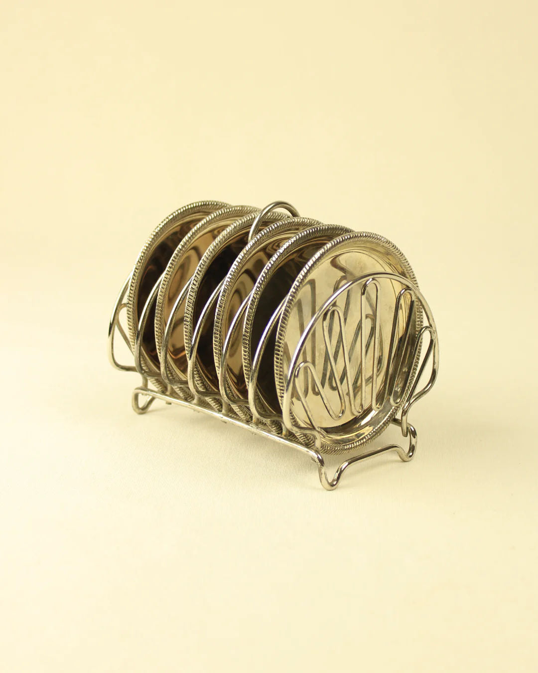 A shell-shaped rack holding a collection of neatly organized silver and black Boga Avante Shop bread plates with a delicate, intricate Art Nouveau style design on a beige background.