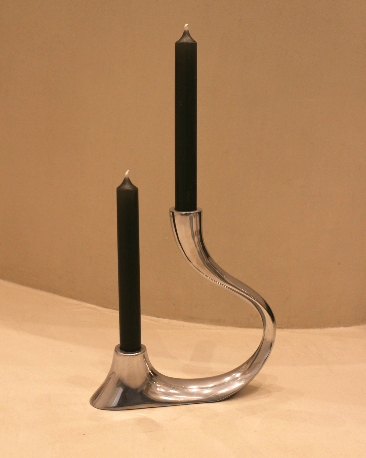 A modern metal Vintage Home Accessories candle holder with a curved design, holding two unlit black candles against a neutral background. The candle holder forms an abstract shape, adding an artistic touch to the setup.