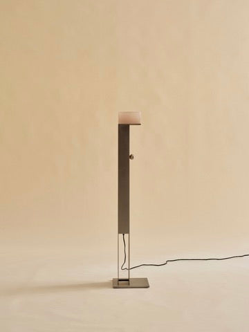 The Perceptions Floor Lamp by Known Work features a sleek, tall dark metal stand and a flat square light against a neutral backdrop. A visible black power cord emerges from the base.