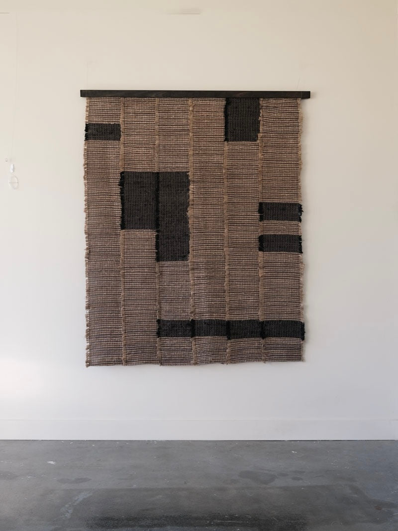 Handwoven textile wall hanging with geometric black patterns on natural burlap