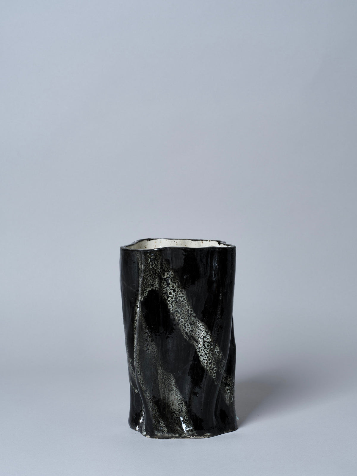 The Swirly Vase Black and White by Astrid Öhman is a handmade black ceramic vase with a glossy finish and abstract, swirling silver patterns, featuring a slightly irregular cylindrical shape and set against a light gray background.