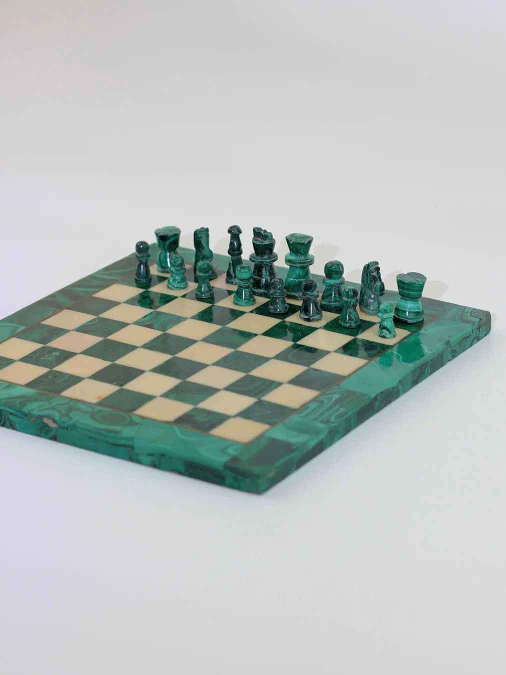 A green and beige chessboard crafted by Boga Avante Shop is shown from a side angle, featuring the intricately carved handmade pieces of the Malachite And Marble Chess set. The glossy set captures the pieces partway through a setup, highlighting its potential as a vintage treasure.