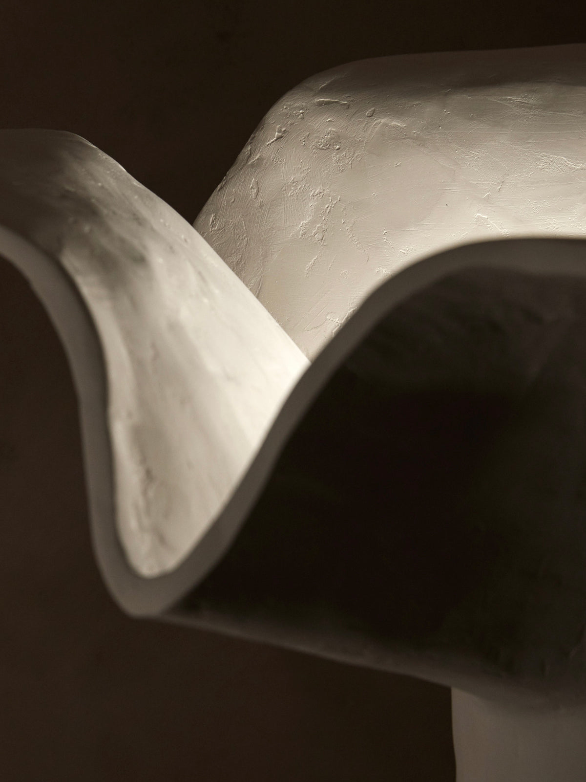 Close-up of a sculpted, abstract white form with smooth, flowing curves and a textured surface, resembling floral silhouettes or waves. Lighting highlights its contours against a dark backdrop, echoing the elegance of Studio Tristan Kallas's 'La Fleur' Table Lamp.