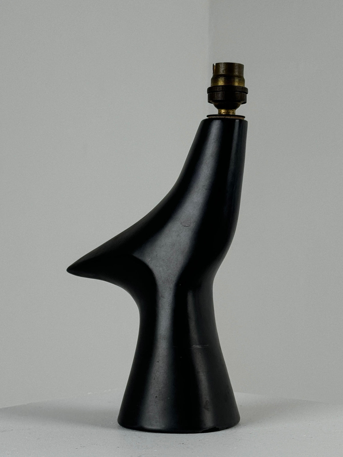 The Zoomorphic Ceramic Lamp by Figuresdesign is crafted with a sleek, sculptural design in black glazed ceramic, reminiscent of modern art. Its smooth, flowing curves and asymmetrical shape draw inspiration from the style of 1960s France, all set against a neutral background.