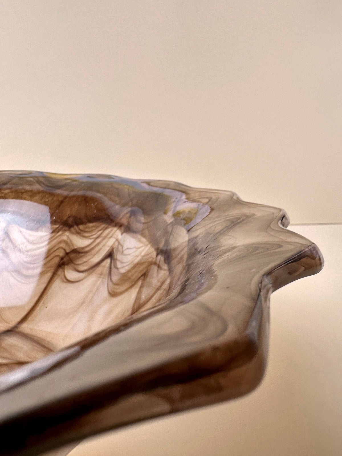 A close-up of a decorative German Art Deco Cloud Glass Bowl with a pointed rim from around 1930. The collectible bowl, by Dodo Vintage, features a smooth, marbled pattern in shades of brown and cream, creating an elegant and artistic look. The background is simple and light, making the bowl the focal point of the image.