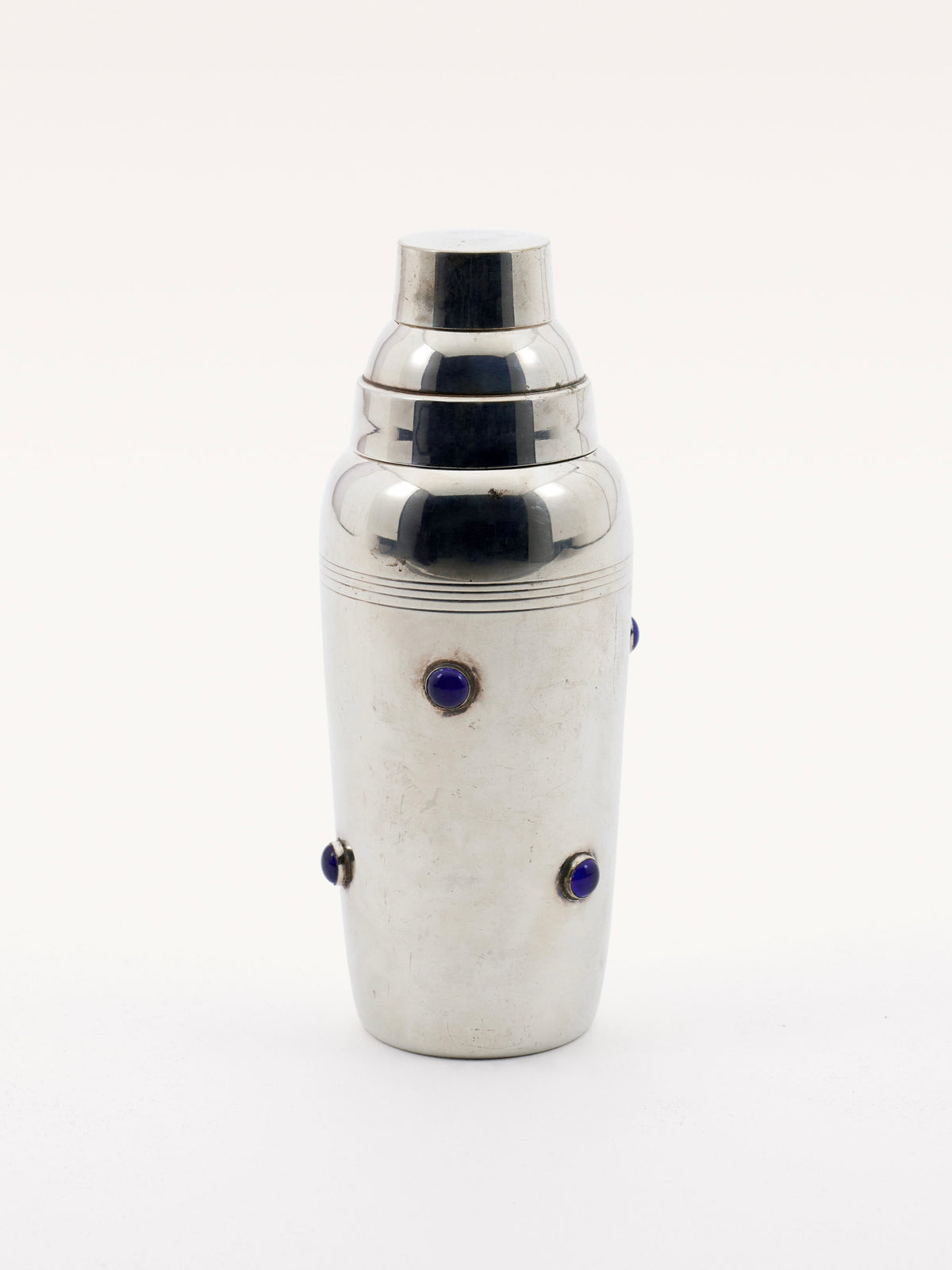 The Shaker with Blue Stones by Galerie MLS features an elegant chrome design, adorned with evenly spaced small blue gemstones. It boasts a smooth reflective finish and a classic, curvaceous shape complete with a detachable lid reminiscent of Cartier style.