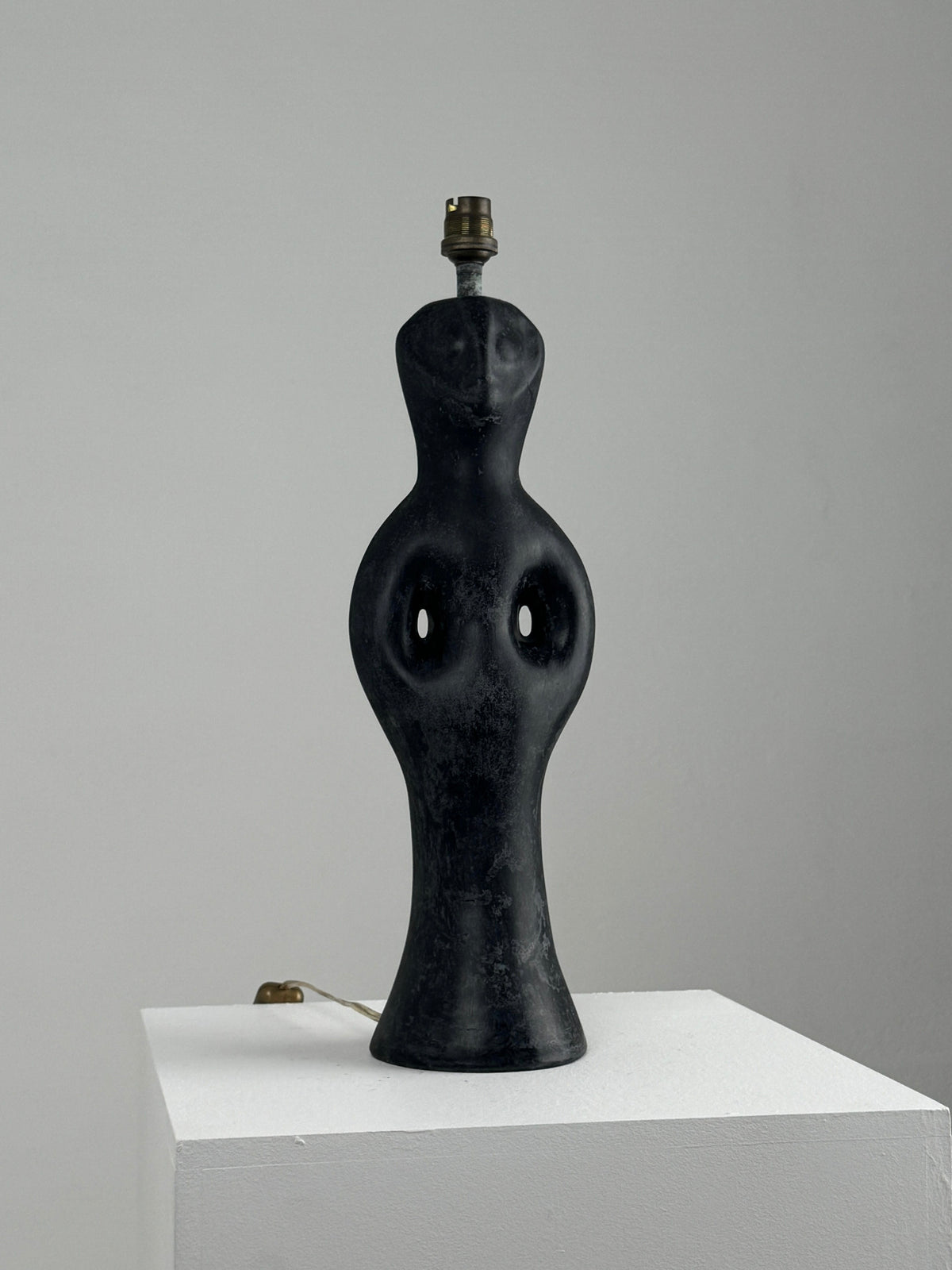 A Black Marble Anthropomorphic Table Lamp by Figuresdesign, styled like a 1950s human figure with a round base and narrow top, elegantly sits on a white pedestal against a plain gray background.
