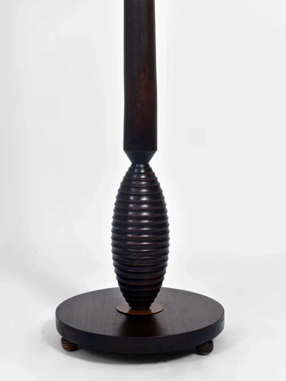 Featuring a closely detailed view, this piece from Barracuda Interiors, the Dark Wooden Floor Lamp, 1930s edition, exhibits an intricately carved ribbed design reminiscent of classic French craftsmanship. It is elegantly mounted on a round base with small feet and boasts a dark polished finish set against a plain white background.