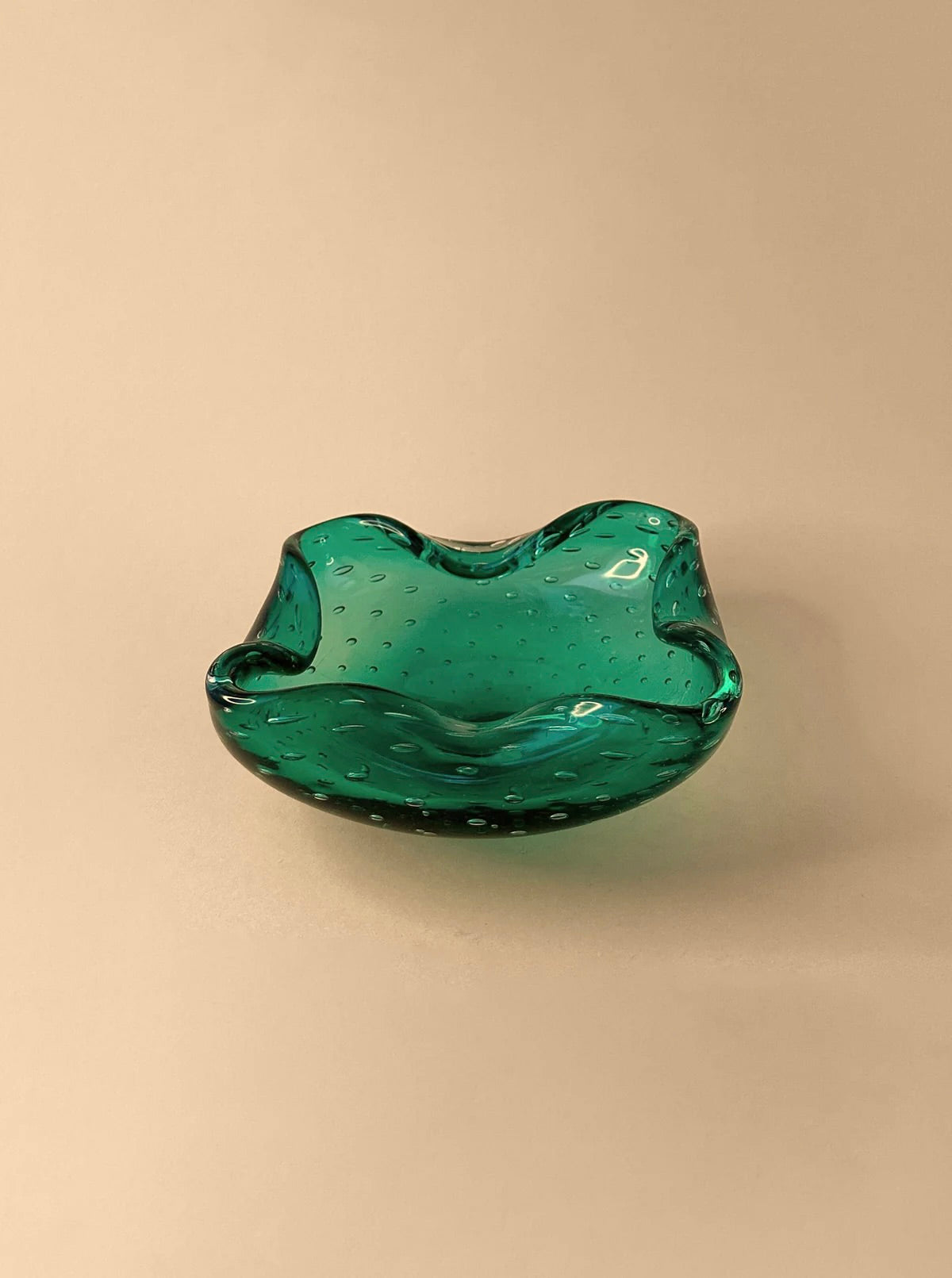 A Mint Green 1960s Murano Ashtray by Dodo Vintage, featuring a wavy, scalloped edge and a smooth, glossy surface, sits on a beige background. This exquisite bowl-like ashtray showcases the bullicante technique with small air bubbles trapped within the glass, adding texture and depth to its appearance.