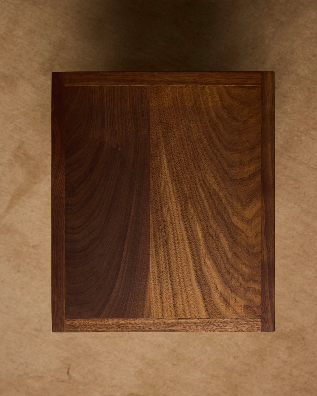 The Jura Pedestal by Ah Um Design Studio is a rectangular handcrafted wood piece with visible grain patterns and a smooth finish, shown from above on a brown textured surface, evoking a brutalist display stand.