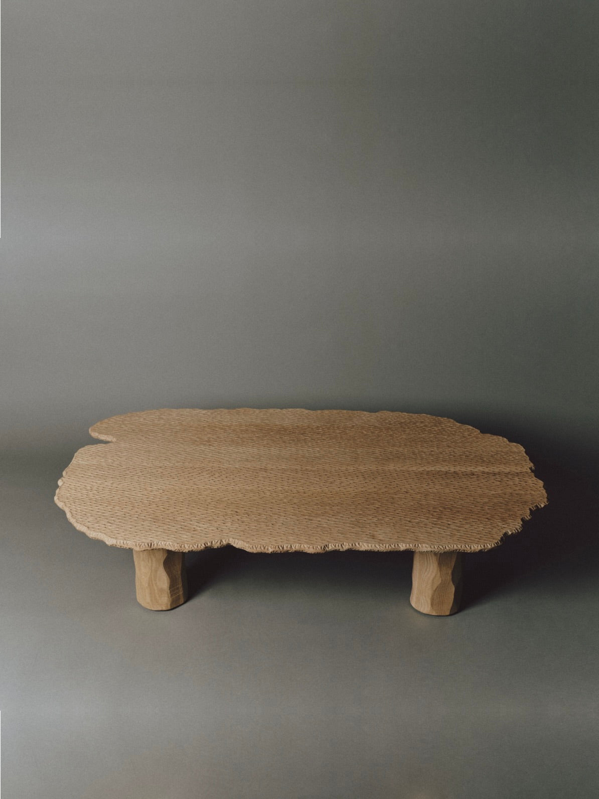 The Mare Coffee Table by Ombia Studio features a low, hand-carved white oak form with an organic-shaped top and three chunky legs, shown against a neutral gray background—an elegant solid wood statement piece.