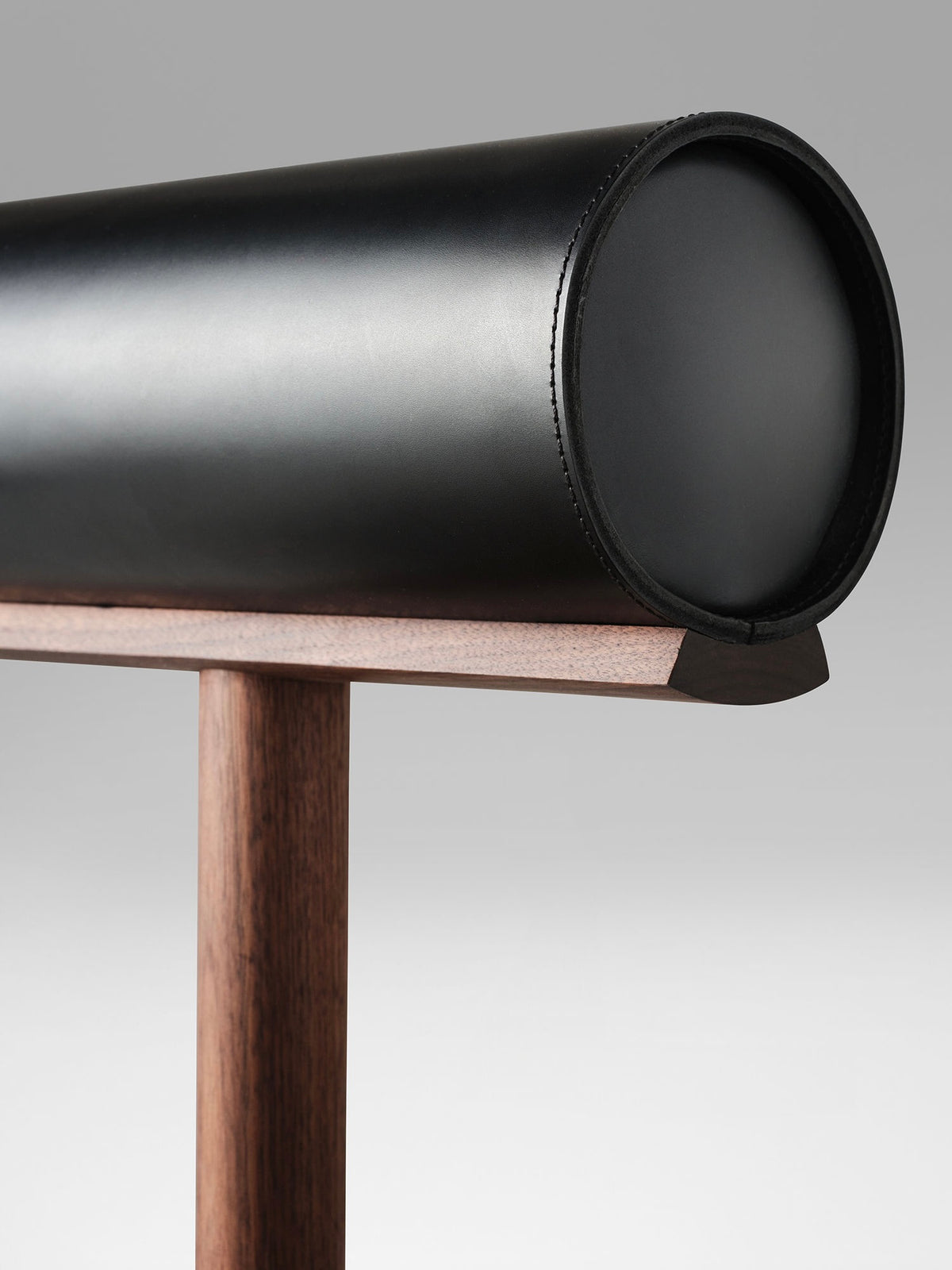 Close-up detail of UNA counter stool's black leather curved backrest and wood base