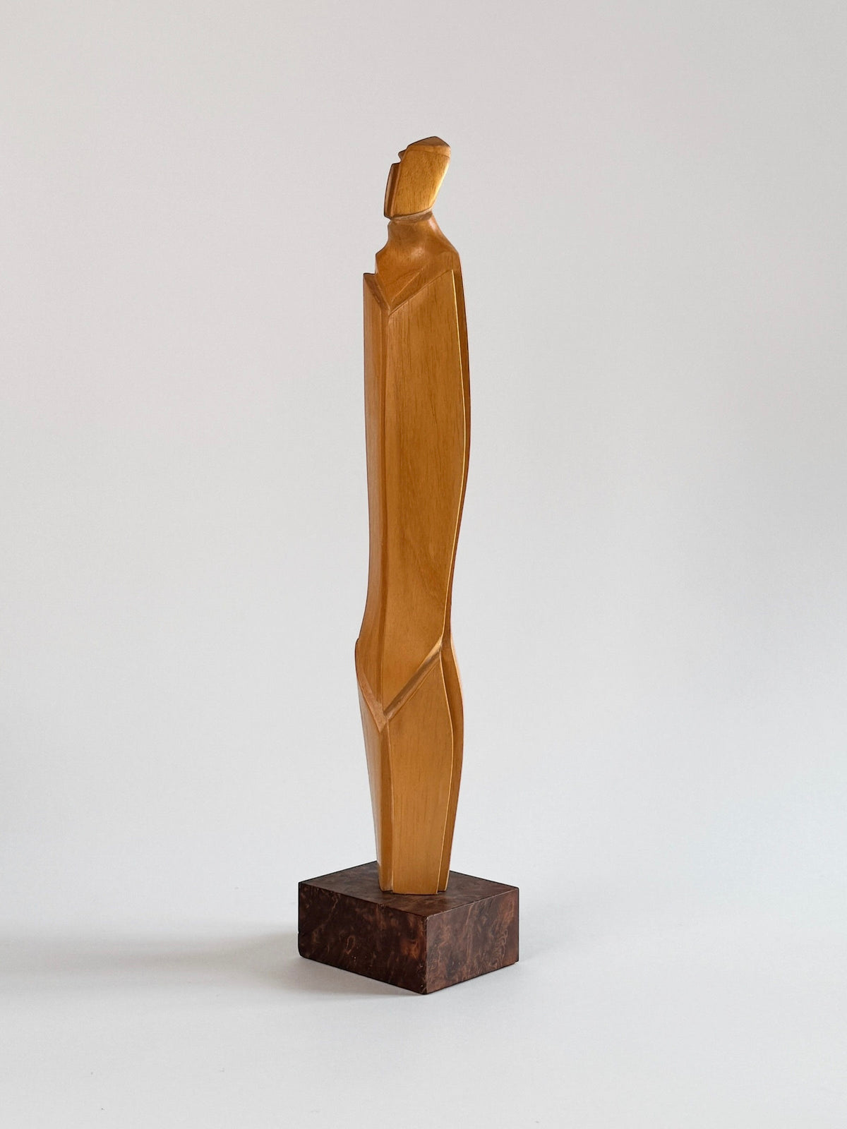 Crafted by Figuresdesign, this Light Wood Sculpture by Pierre Dedieu showcases a tall, abstract human form with simplified geometric lines and a smooth finish. It stands elegantly on a dark square base, set against a plain background.