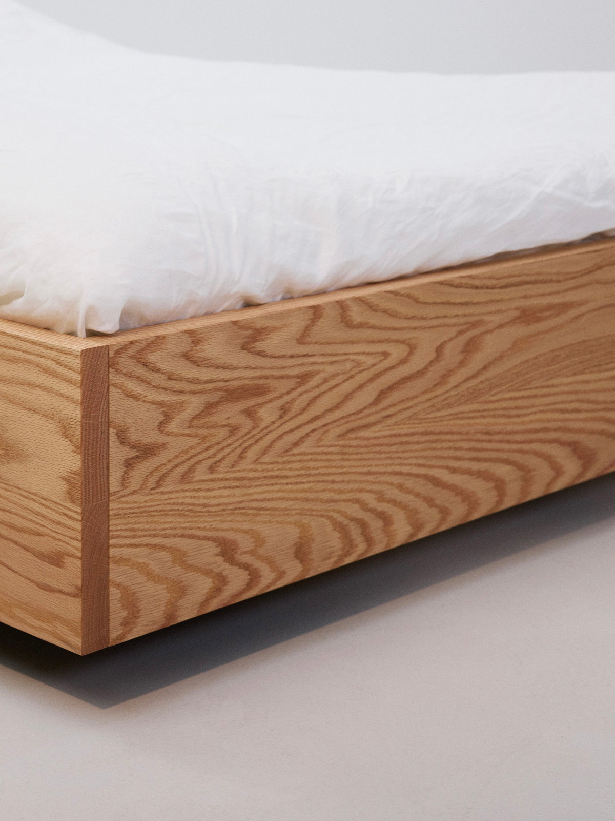The Floating Bed - Natural by Axel Wannberg features a minimalist Red Oak frame with a light wood grain finish and a white mattress, set against a plain background.