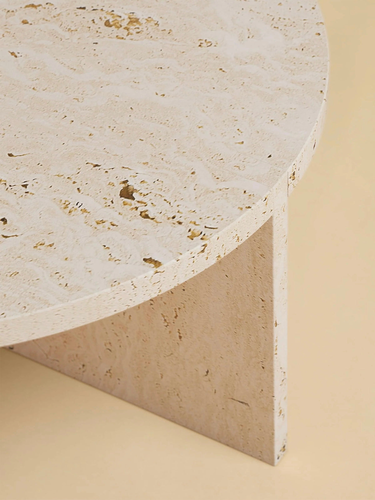 Close-up of the "Hashi" Coffee Table in Marble by Lebanto, featuring natural stone textures and a thick triangular base. The light beige surface showcases unique patterns against a soft pastel background.