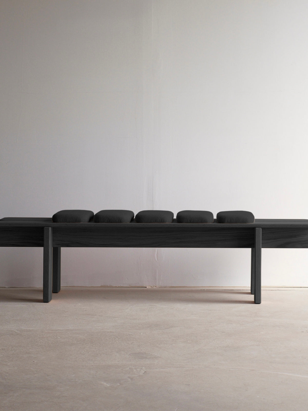 The Ueno Bench Black Edition by malva, a minimalist solid oak design with five small cushions, rests on a light floor against a plain white wall, highlighting modern aesthetics and Japanese craftsmanship.