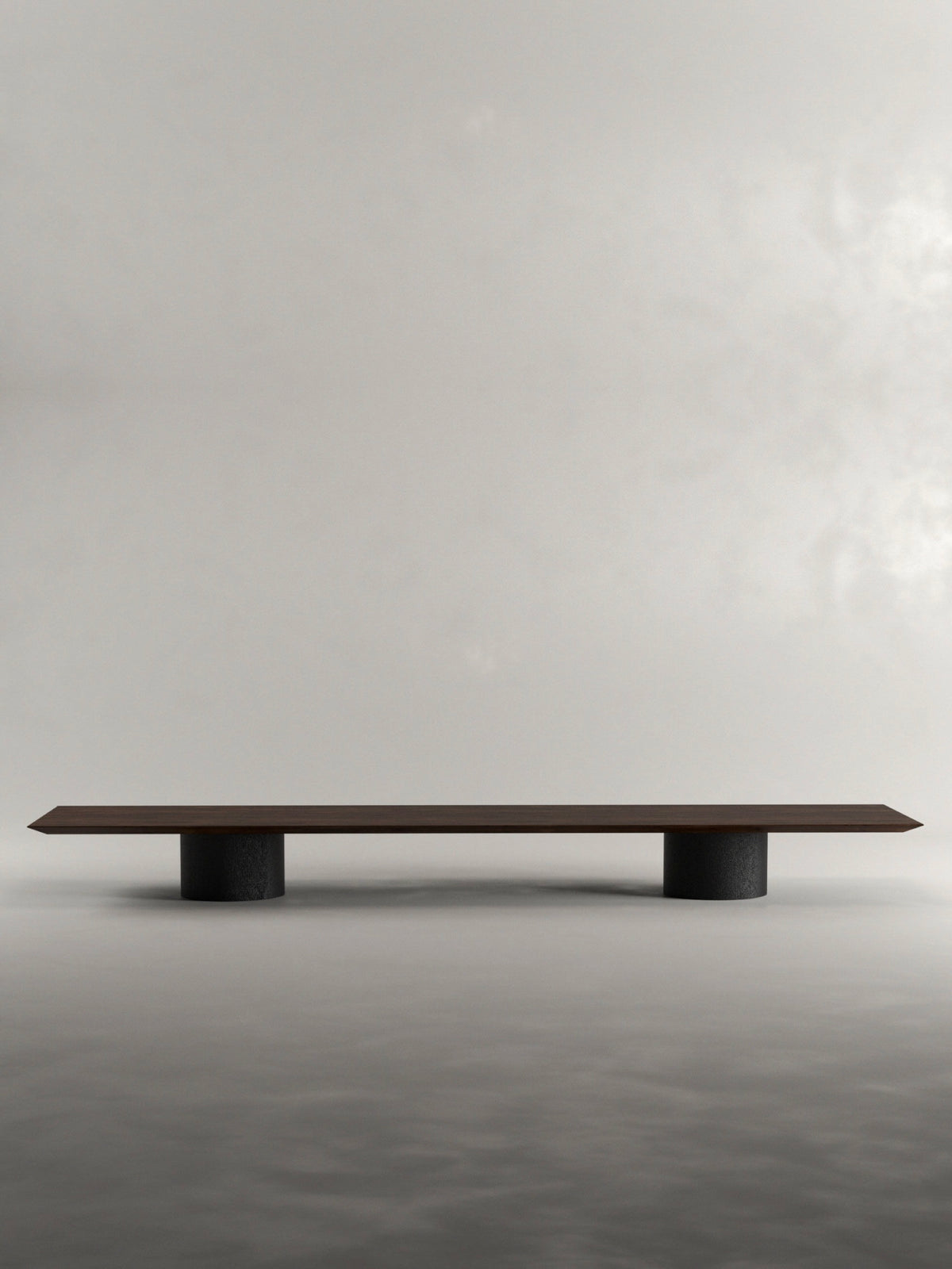 The 'Pier' Coffee Table by Siete Studio features a minimalist design with a solid black oak top and pillar bases, set against a cloudy, muted backdrop. Its sleek form highlights simplicity and modern elegance.