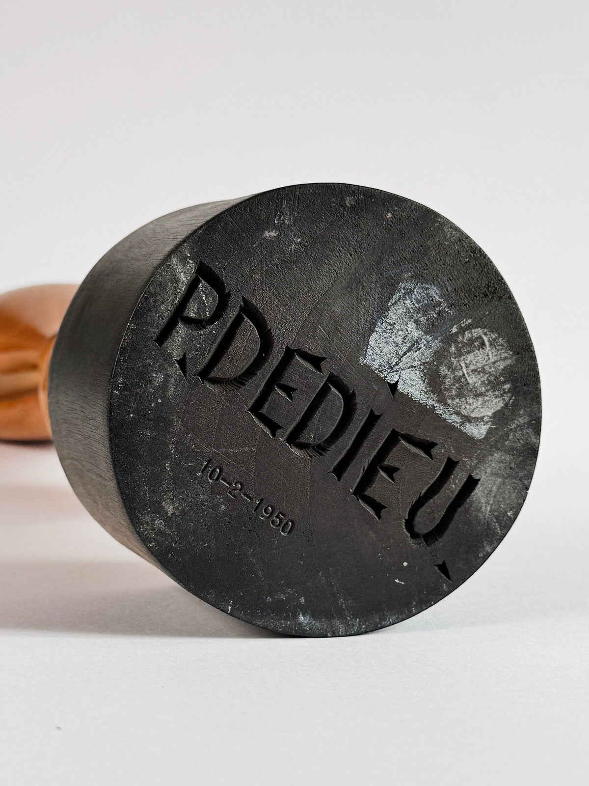 A wooden-handled rubber stamp with the carved text "PDEDIEU" and the date "10-2-1950" beneath it sits on a white surface, reminiscent of a Wood Sculpture by Pierre Dedieu from Figuresdesign.