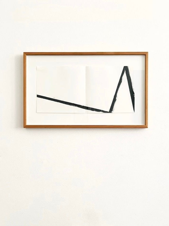 A minimalist artwork, the Richard Nonas Original Lithograph by Médecine, sits in a wooden frame on a white wall. The piece showcases black lines forming an abstract geometric shape, reminiscent of a right triangle and straight lines on a white background, capturing the essence of Richard Nonas' post-minimalist style.