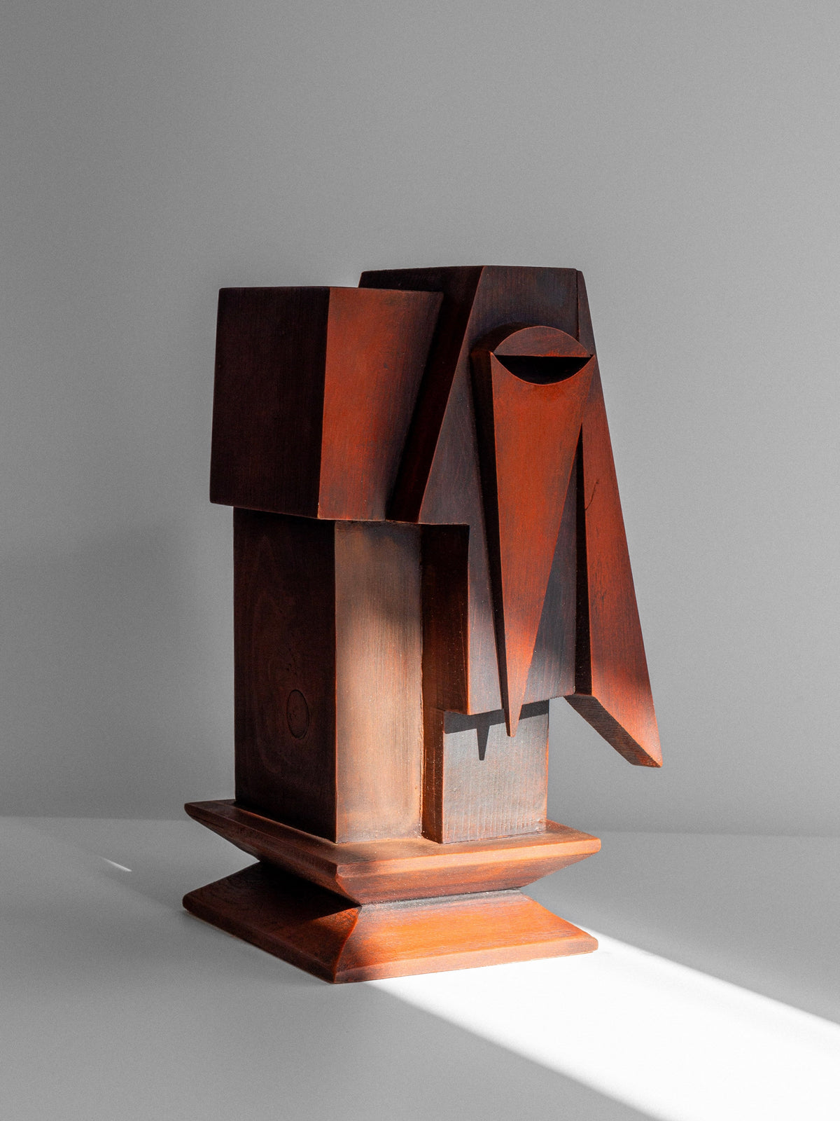 A Vintage Cubist Sculpture by Atelier Boulogne from Spigel, composed of wooden geometric shapes, sits on a flat, white surface. This contemporary minimalist piece features a combination of rectangular and triangular forms in varying shades of brown, reminiscent of cubism. Sunlight casts a soft shadow on the sculpture.