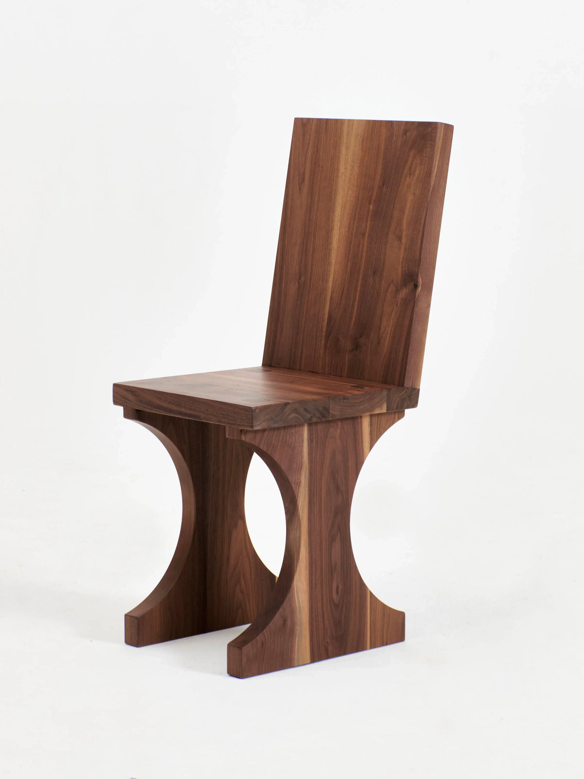 Introducing the Portugal Chair No 3 by Project 213A: a modern wooden chair with a minimalist design, featuring a rectangular backrest and seat. The legs consist of two curved, semi-circular supports, combining aesthetic appeal with structural elegance. Handcrafted in Portugal from solid walnut, this piece boasts a rich, natural finish.
