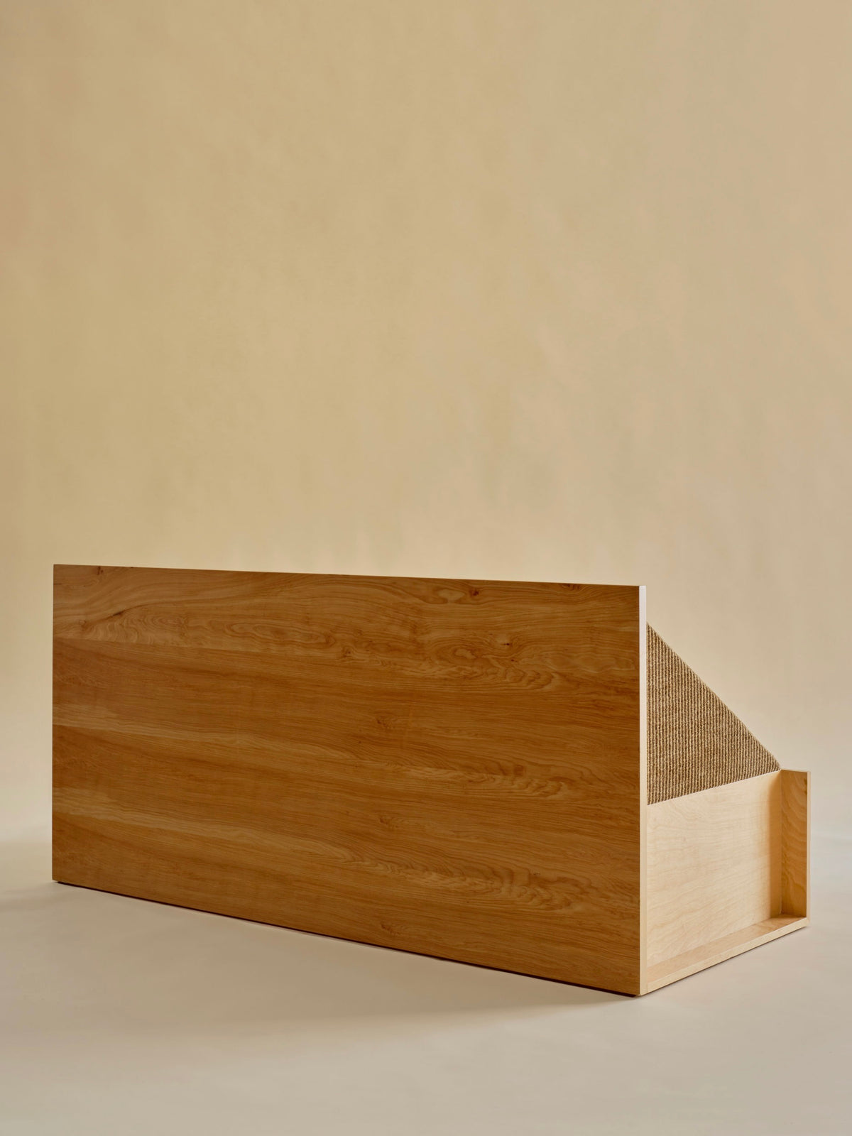 The 'Perceptions' Sofa Bench by Known Work features a sleek, minimalist wooden design with a rectangular base and slanted top adorned in textured upholstery, standing elegantly against a beige background to embody minimalist values.
