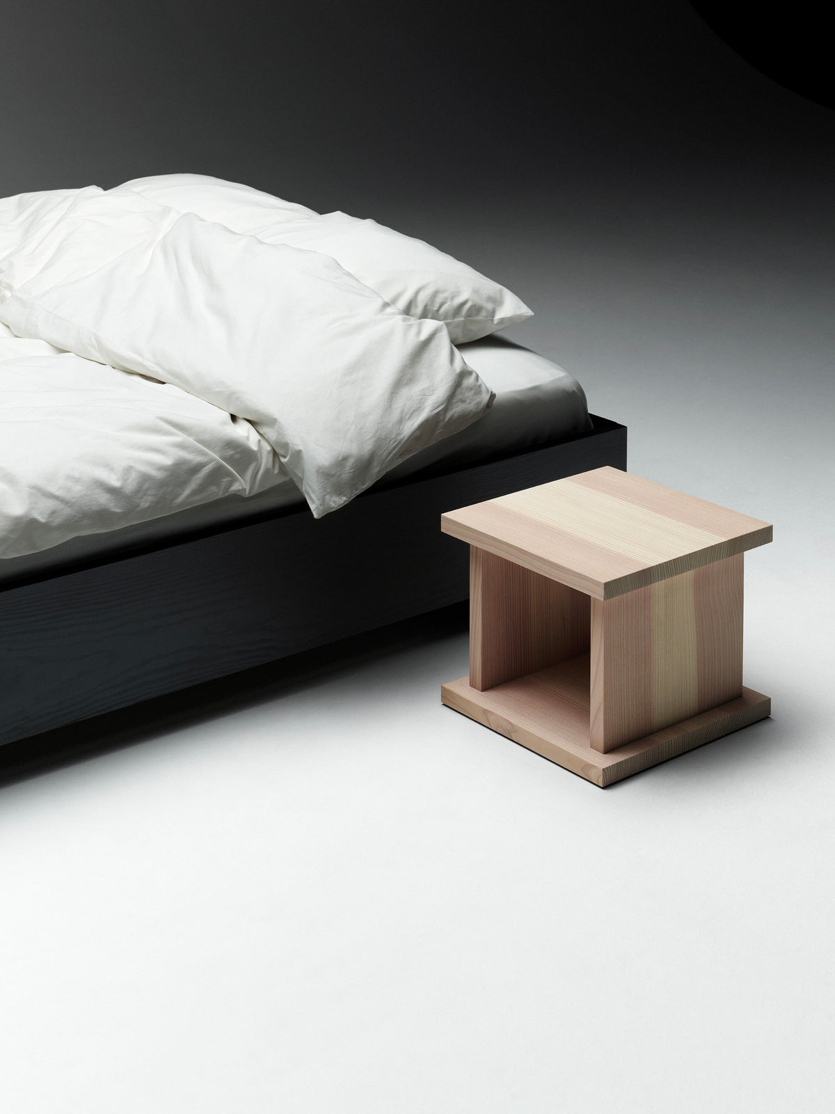 Black floating bed with white bedding and wooden bedside cube