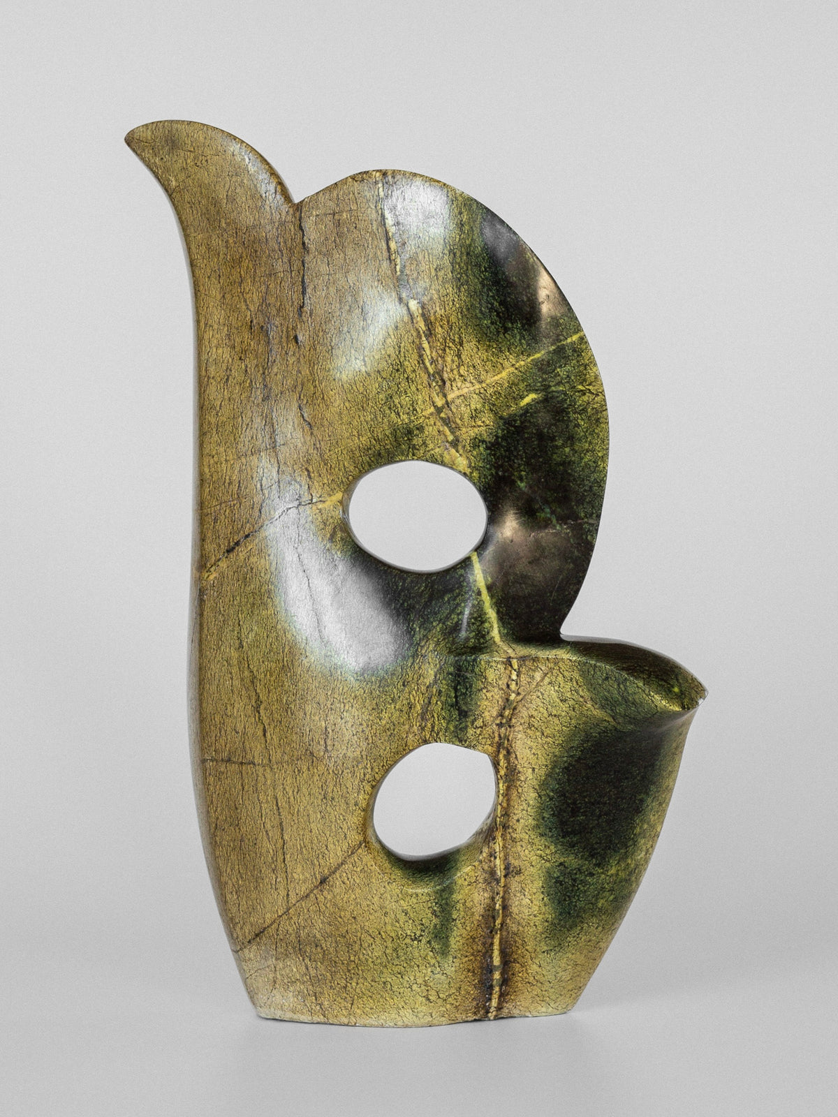 The Abstract Stone Sculpture II by Spigel is a polished work by a talented Zimbabwean artist, exhibiting a smooth curved form with circular cut-outs. Made from leopard stone, it has a greenish-gold hue and visible veins, resembling a stylized bird on a gray background.