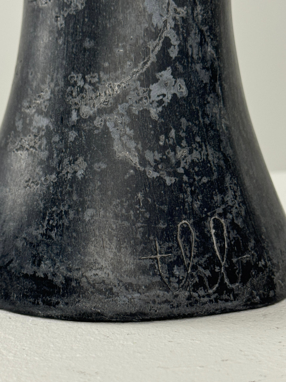 The textured base of a Black Marble Anthropomorphic Table Lamp by Figuresdesign features a worn, speckled surface with "tll" initials etched into it. Resting on a light-colored surface, this vintage piece exudes 1950s charm.