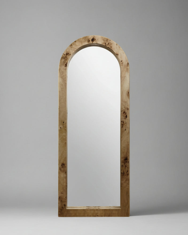 A Ransom & Dunn Arc Burl Wood Floor Mirror, featuring a natural ash burl wood frame, stands upright against a neutral beige background, exuding a subtle nod to neoclassical architecture.