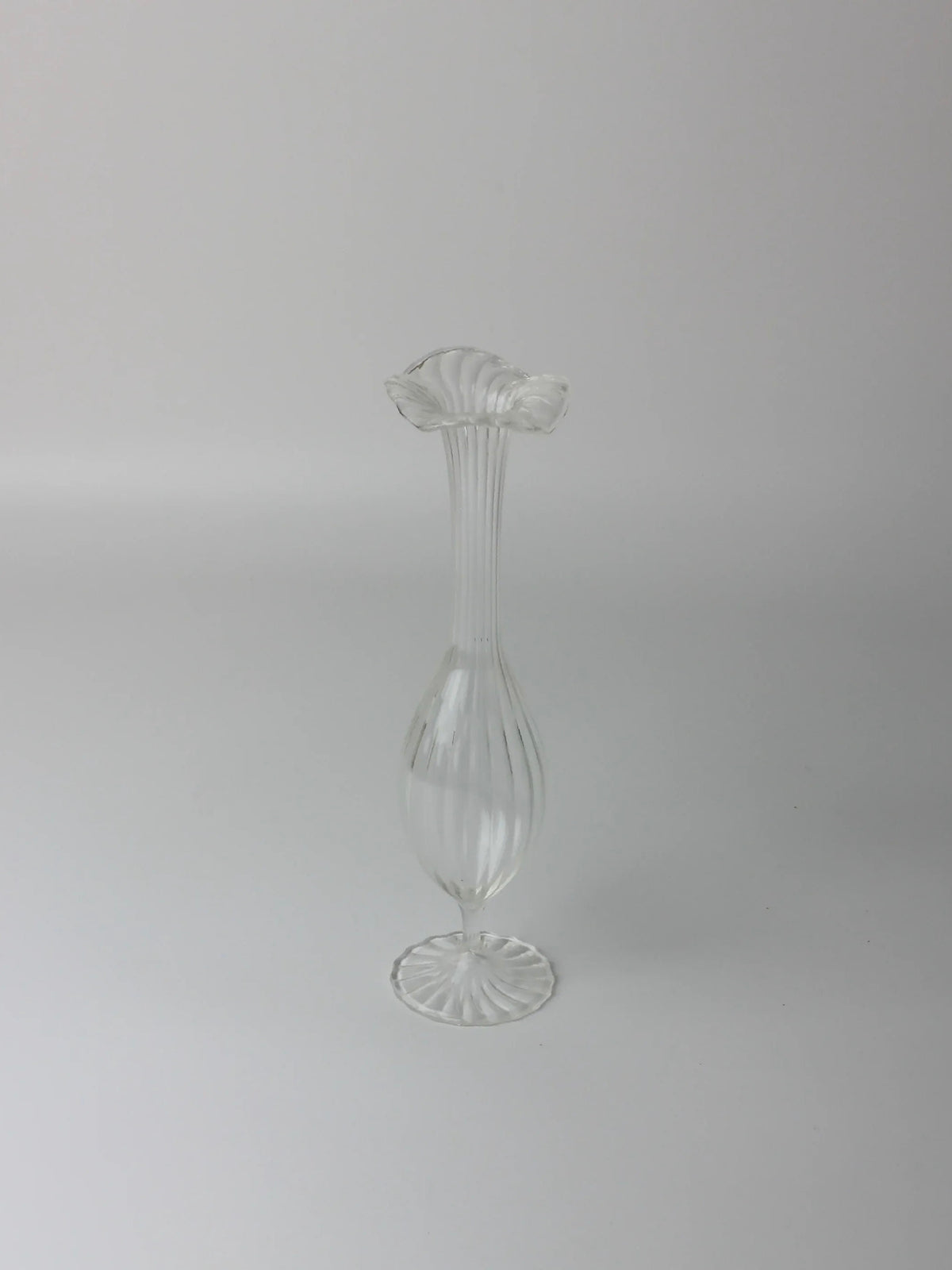 The Pair of Murano Candle Holders by Boga Avante Shop features a slender, elegant shape with vertical grooves and a wide, scalloped top reminiscent of vintage blown glass. Their classic design and clear glass finish echo timeless style against any backdrop.