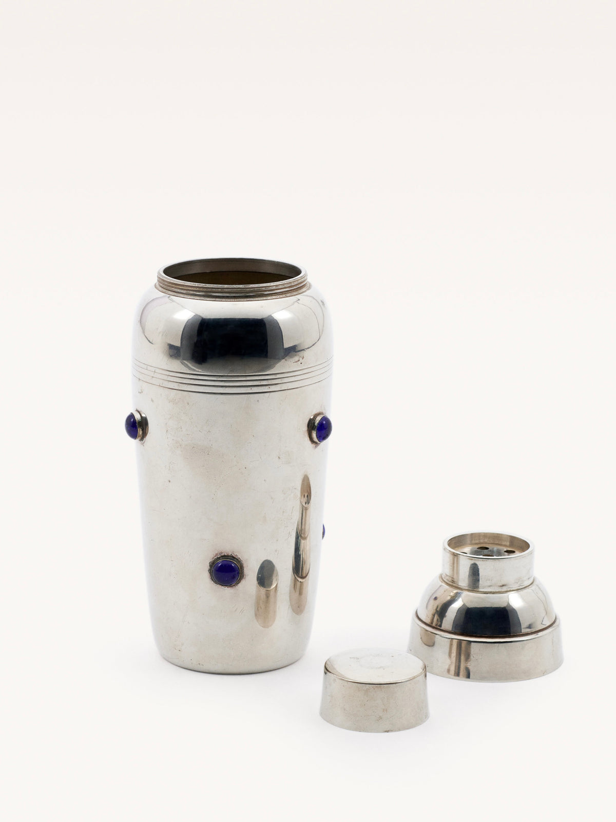 A sleek Shaker with Blue Stones by Galerie MLS features a chrome cylindrical body with Cartier-style blue stone accents. The lid and cap are beside it, displaying the open shaker against a plain white background.