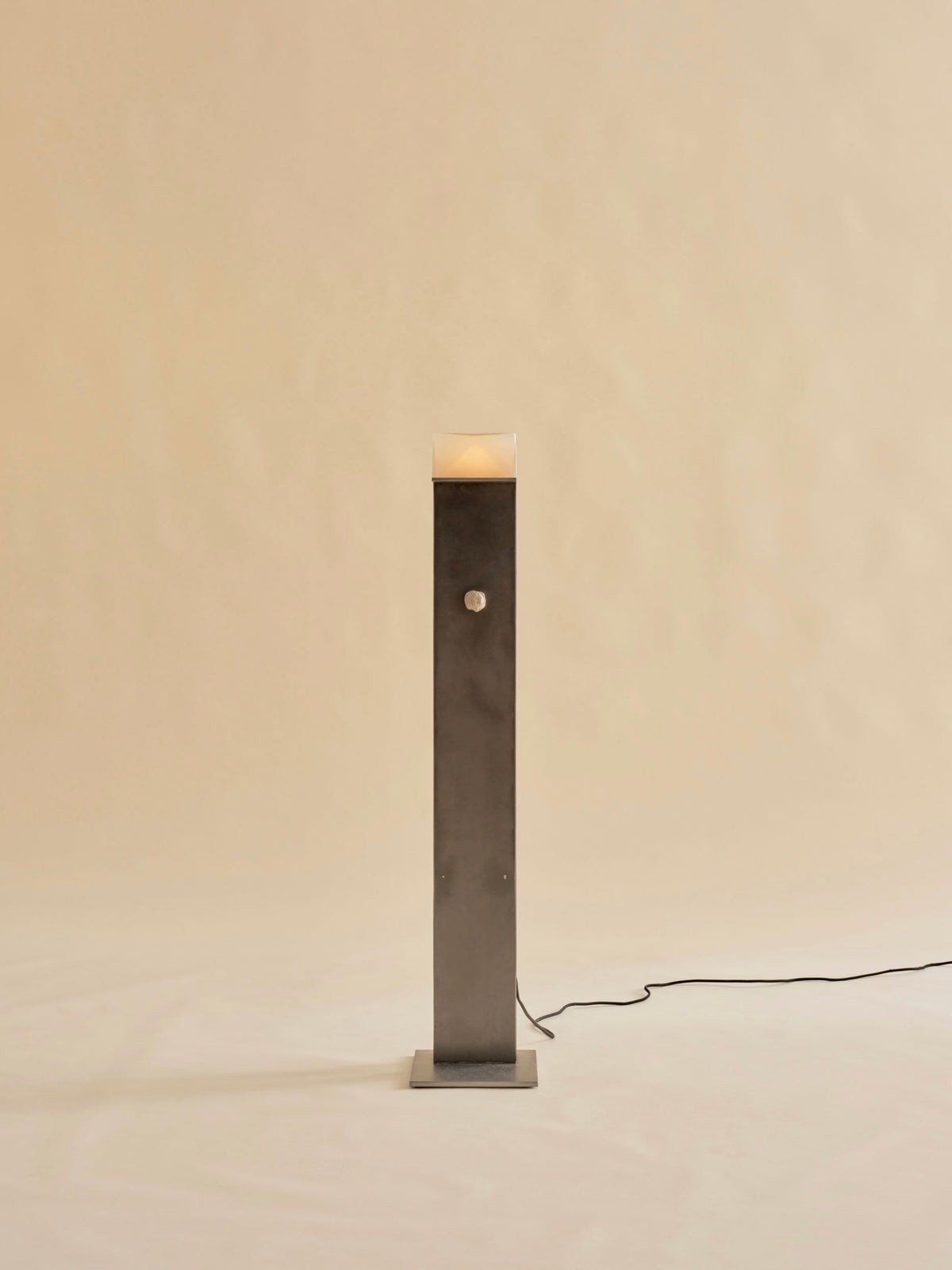 The Perceptions Floor Lamp by Known Work features a tall and slender dark metal design on a simple square base against a beige background, with a handcrafted spherical knob midway and connects to power via a black cord.