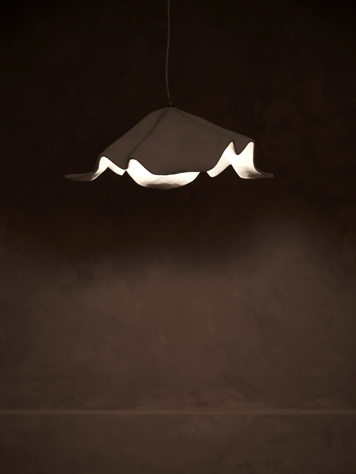 Studio Tristan Kallas's 'La Fleur' Pendant Light hangs elegantly, its ruffled design casting a soft glow and dimmable to create gentle shadows, enhancing the ambiance with its unique shape.