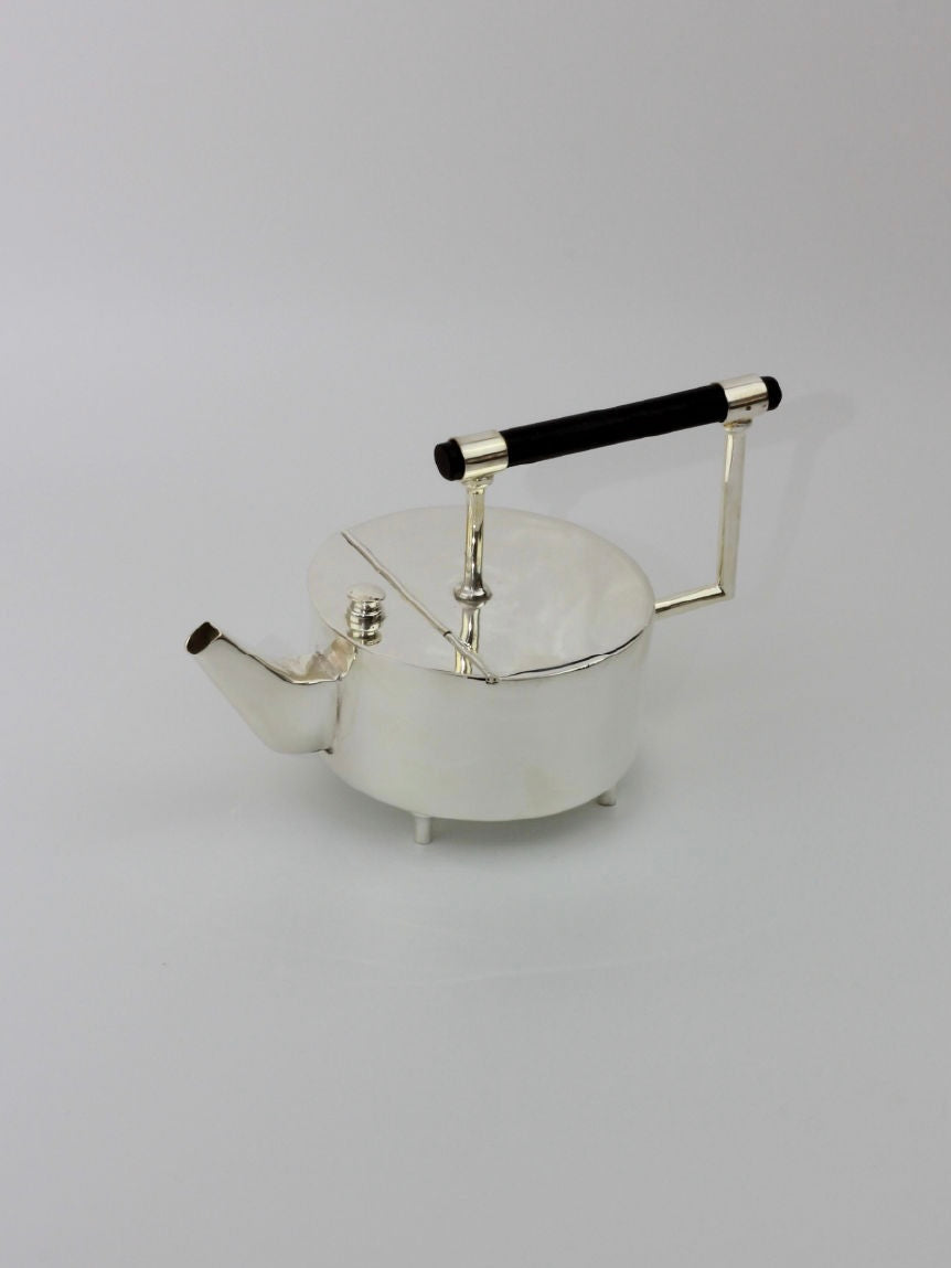 Introducing the Christopher Dresser's Tea Pot by Boga Avante Shop: a sleek, silver-plated marvel with a modern cylindrical body, a short spout, and a knobbed lid. It features an elegant ebonized wood handle attached to metallic arms and stands sturdily on four small feet against a pristine white background. This design pays homage to the iconic style of Dr. Christopher Dresser.