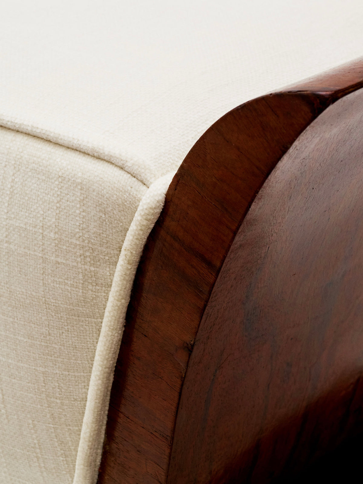 Close-up of a bed corner featuring a curved 1930s walnut frame and beige textured fabric, similar to the elegance of Galerie MLS's Art Deco Stool. The wood offers a rich, smooth finish with the fabric adding a soft contrast.