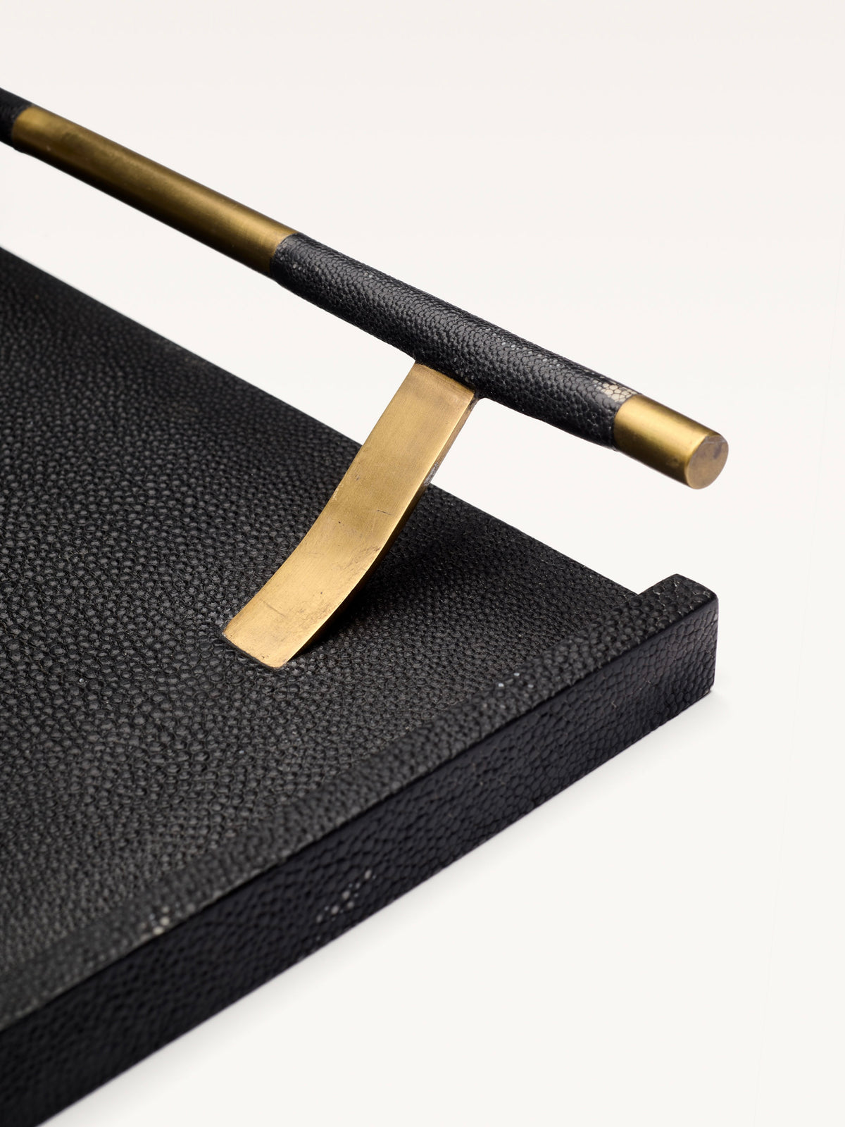 Close-up of the Galerie MLS Black Shagreen Tray, featuring a bronze patina brass handle partially wrapped in black material and supported by a curved brass bracket, set against a plain white background.