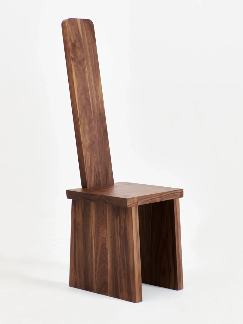 The Portugal Chair No 4 by Project 213A is a modern, minimalist chair crafted entirely from handcrafted walnut. It boasts a tall, narrow graphic backrest, a flat square seat, and thick, angled legs. The chair's clean lines and natural wood grain combine to give it a sleek and elegant appearance.