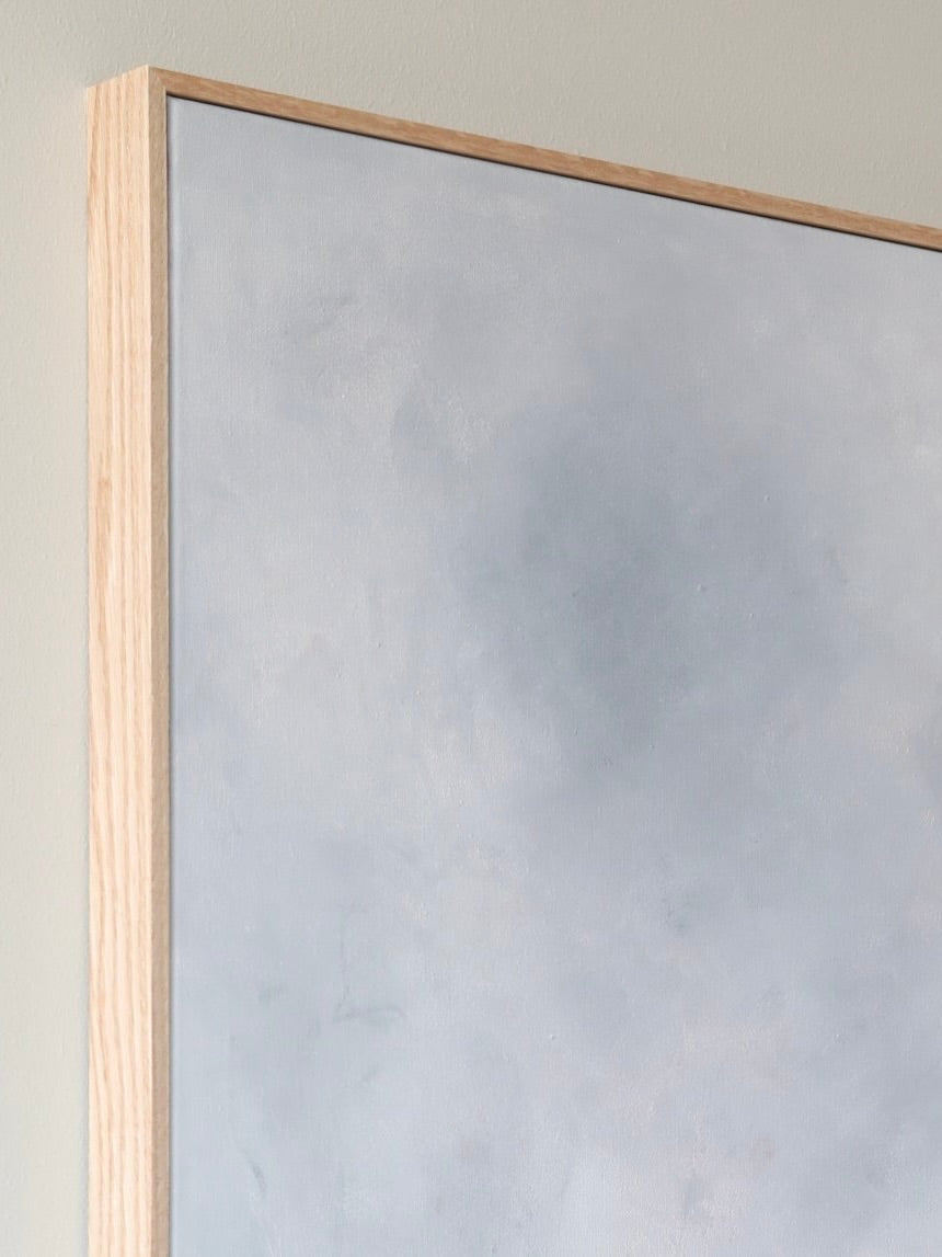 Close-up of the corner of a framed acrylic painting. The oak frame, made of light wood, showcases the canvas art titled "Eos," an abstract design with various shades of gray from A Nesting Place's 2024 collection. The neutral background wall complements the artwork beautifully.