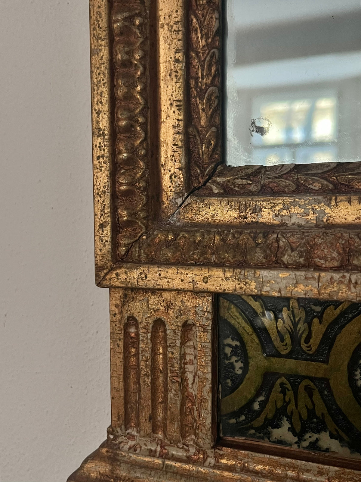 Close-up of the Médecine Antique Gilded Mirror frame, featuring ornate gold and brown carved details, plus touches of green, gold, and black in a neoclassical design; the mirror subtly reflects light.