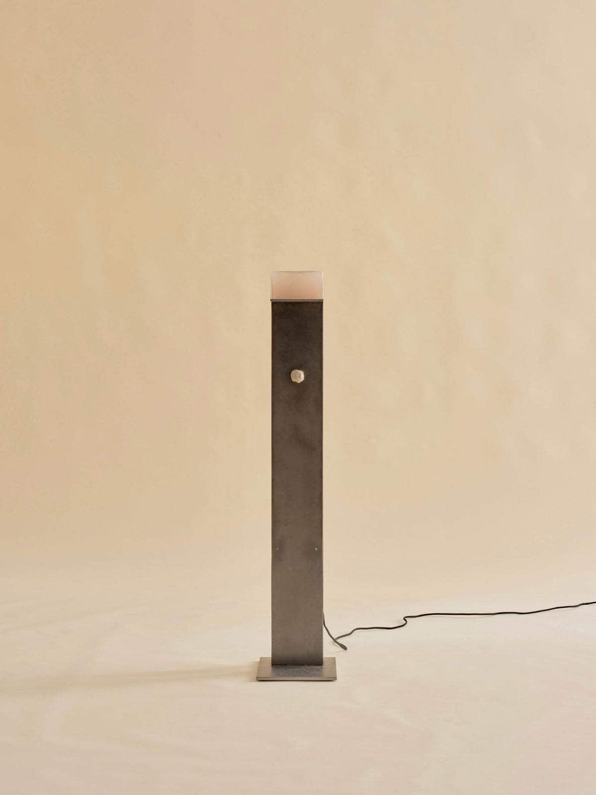 The Perceptions Floor Lamp by Known Work is a tall, sleek rectangular lamp with a metallic finish. Handcrafted with precision, it features a square base and a power cord at the back, set against a plain beige background.