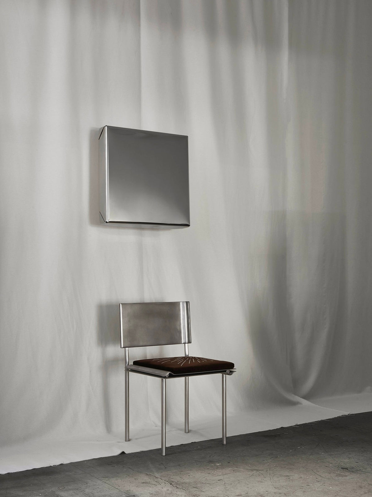 Modern square mirror with metallic frame mounted above minimalist steel chair
