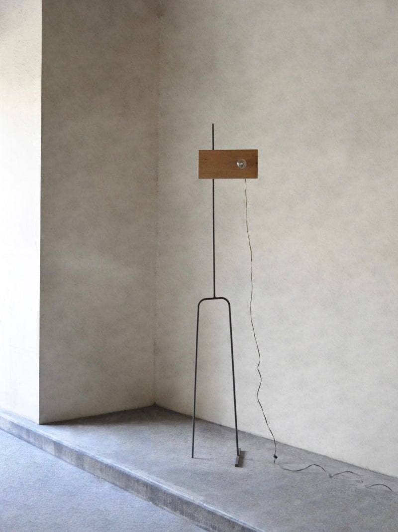 The 'Oiseau' Oak Floor Lamp by Eloi Schultz features a minimalist design with a slim black metal stand, a rectangular oak shade, and an exposed cord that rests on the floor, highlighting its simple, modern aesthetic.