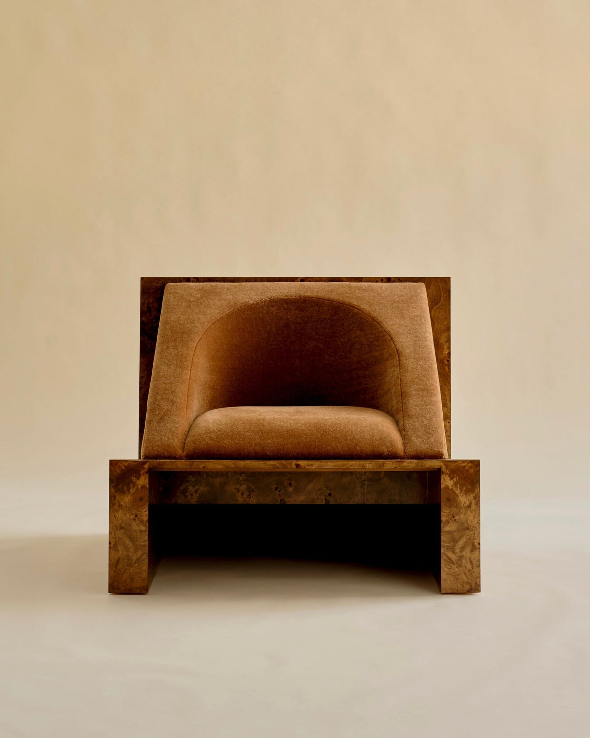 The 'Perceptions' Armchair by Known Work is a minimalist design with a rectangular wooden frame and plush, rounded brown upholstery, set against a plain beige background.