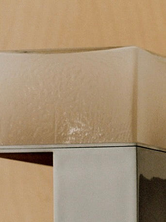 Close-up of a handcrafted beige and gray corner edge guard on a gray furniture piece, showcasing its textured surface contrasting with the furniture's smooth finish.